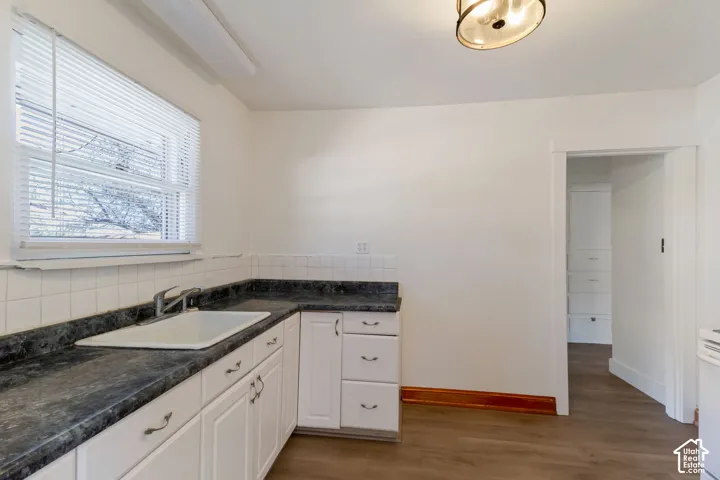 Kitchen featuring white cabinetry, dark countertops, a white tile backsplash, wood-finish flooring, and a ceiling-mounted light fixture
