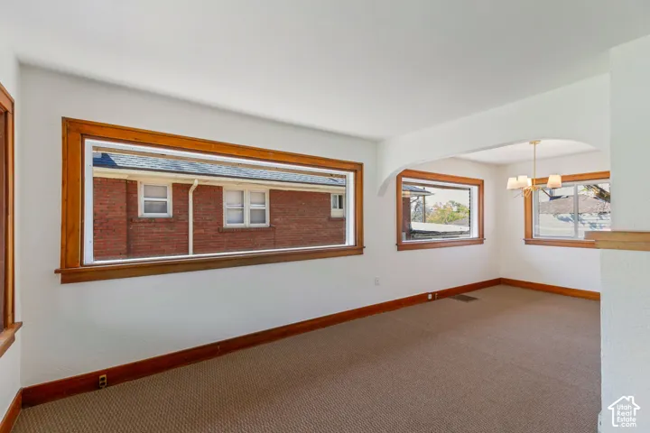 Expansive room featuring multiple windows with wood trim, neutral carpeting, and an arched entry to an adjacent space with a chandelier