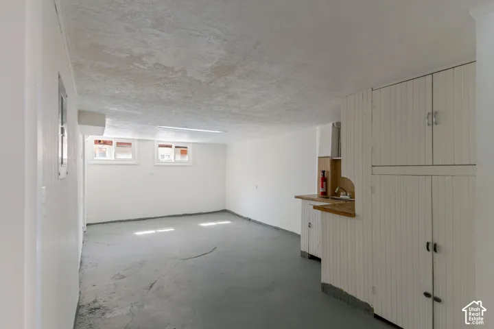 White painted walls, concrete flooring, built-in cabinetry with beadboard paneling, countertop with sink, and natural light from multiple windows