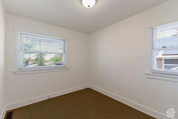 White walls, brown textured carpeting, two windows with white blinds, and a flush mount ceiling light fixture