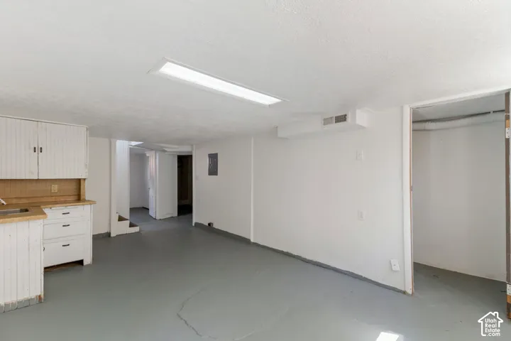 Spacious room featuring a utility sink, white cabinetry with wood-finish countertops, and a built-in overhead fluorescent light fixture