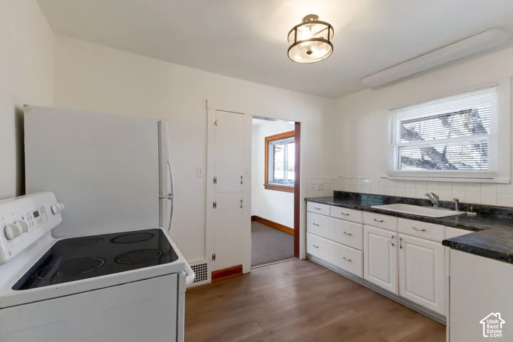 Kitchen featuring wood-finish flooring, white cabinetry, dark countertops, white tile backsplash, and a window above the sink