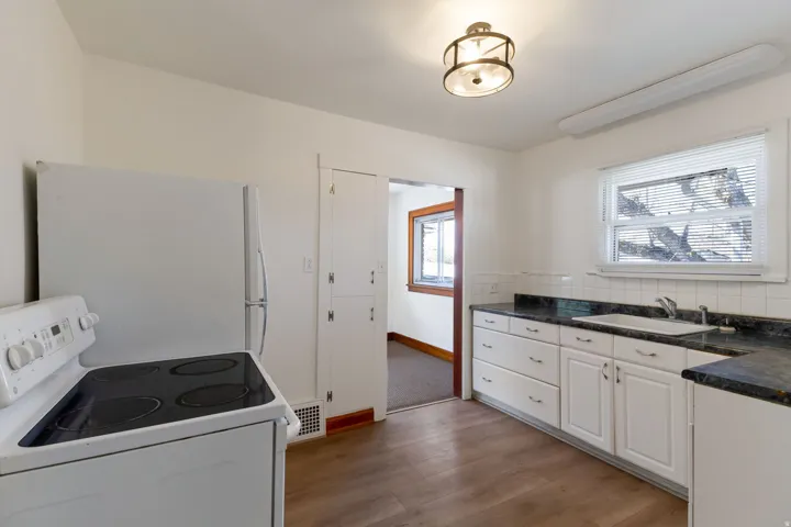 Kitchen featuring wood-finish flooring, white cabinetry, dark countertops, white tile backsplash, and a window above the sink