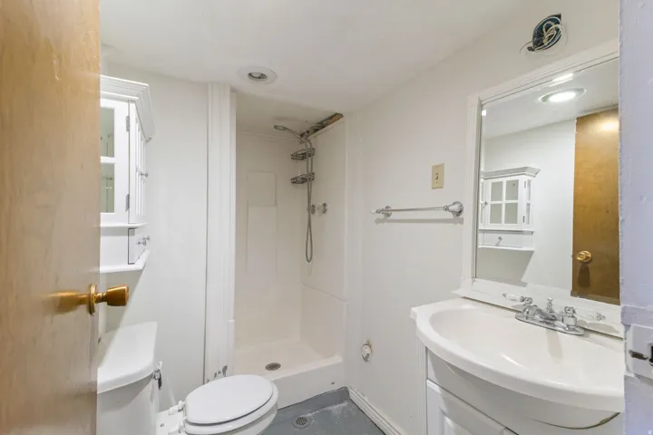 White vanity with integrated sink, wall-mounted mirror, stand-up shower, and built-in wall cabinet