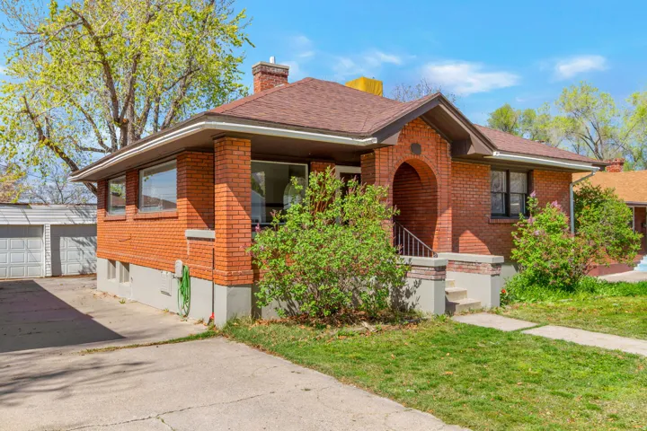 Brick exterior with a covered porch, arched entry, brown shingle roof, and concrete driveway
