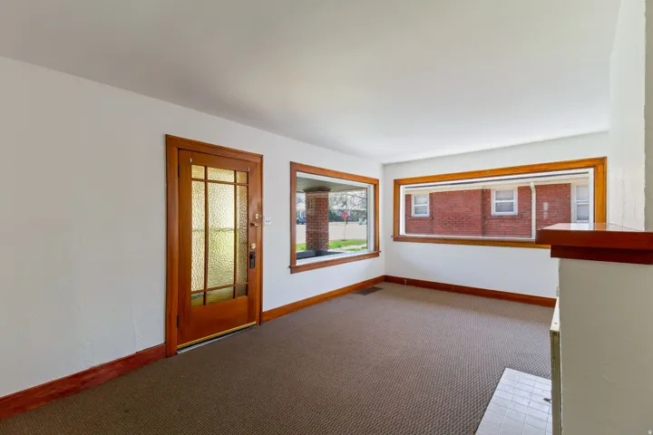 Hardwood trim and baseboards throughout, large picture windows, wood-paneled entry door with frosted glass inserts, and a built-in fireplace hearth with tile surround