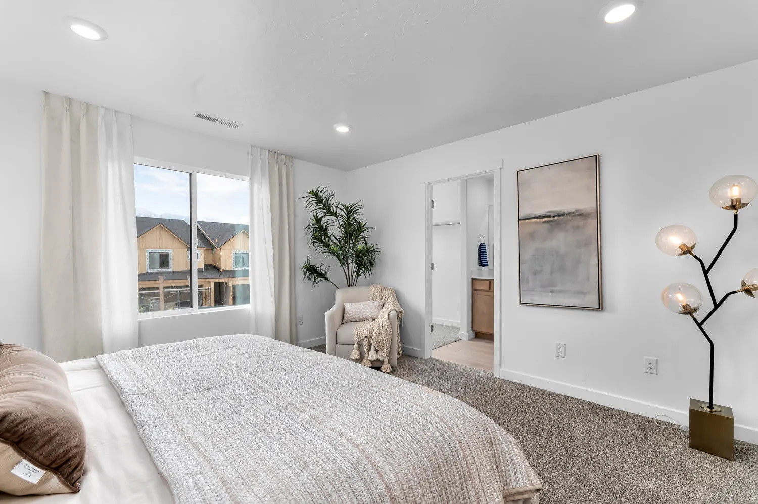 Recessed ceiling lighting, wide window, carpet flooring, white walls, and a visible doorway leading to an additional space with a vanity