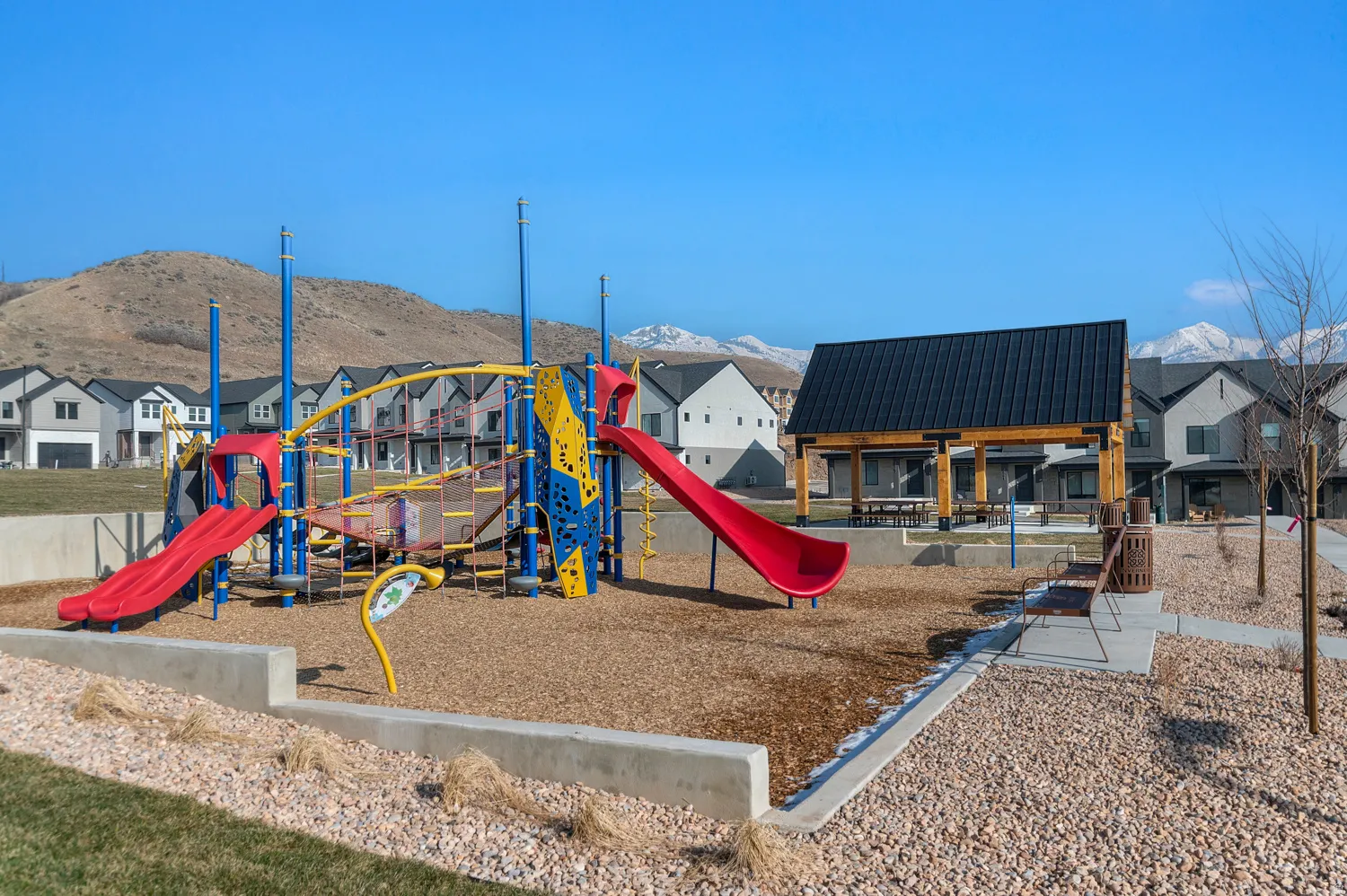 Community playground with a multi-level play structure, two slides, and wood chip surfacing
