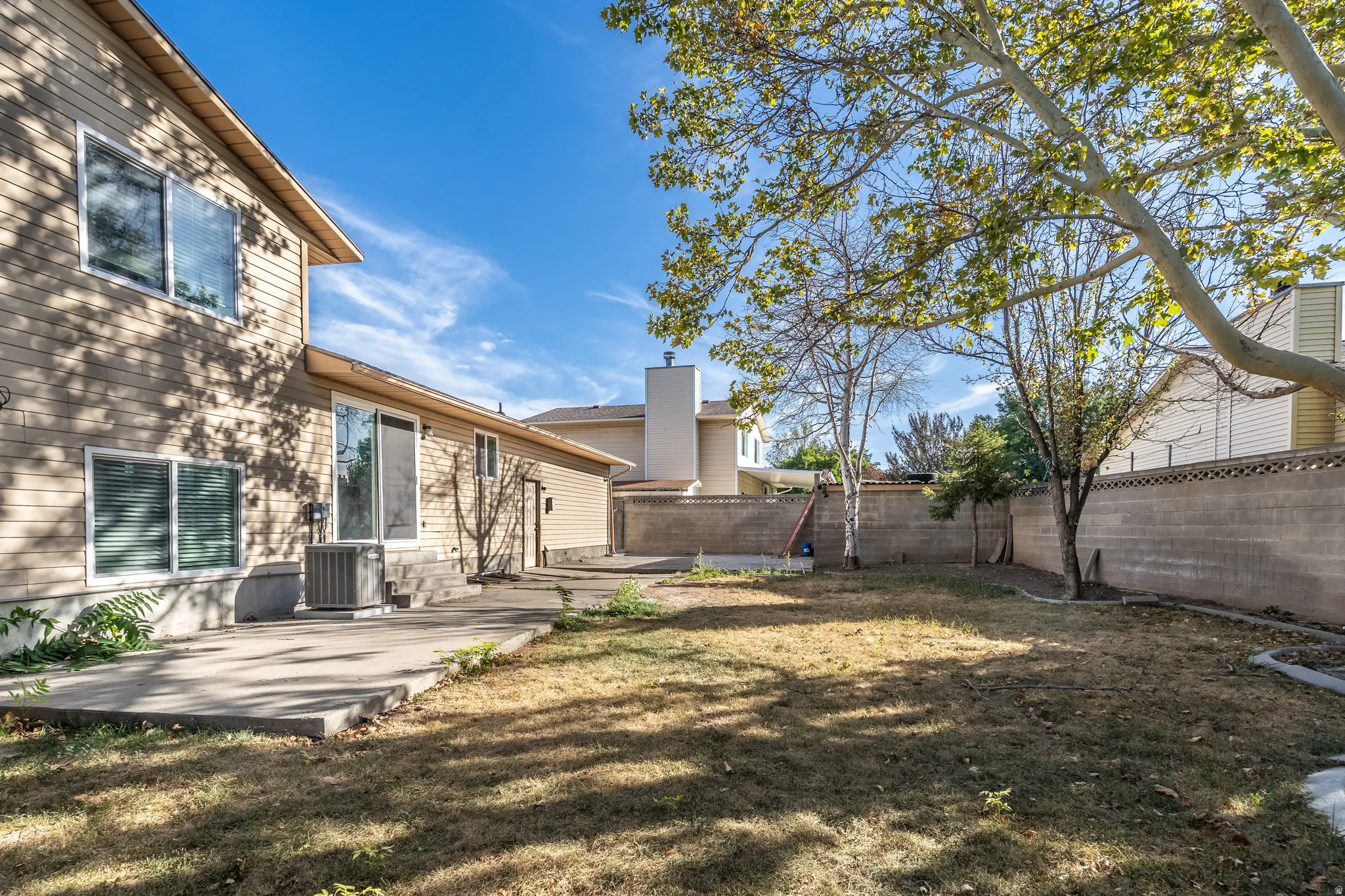 Spacious backyard featuring a concrete patio, mature trees, and a block fence