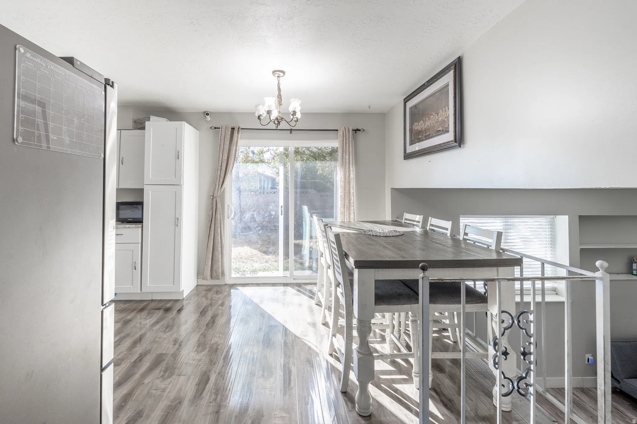 White cabinetry, wood-finish flooring, sliding glass door, overhead chandelier, and a decorative railing
