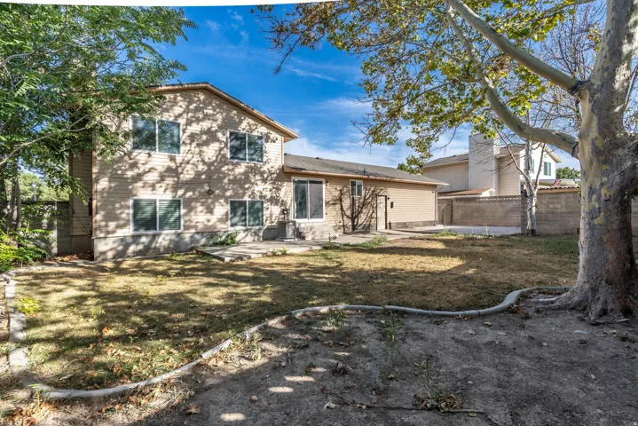 Expansive backyard featuring a mature shade tree, a concrete patio, and a privacy wall