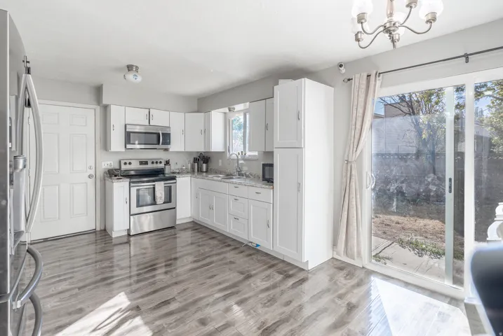 Kitchen featuring white cabinetry, stainless steel appliances, wood-finish flooring, and a sliding glass door