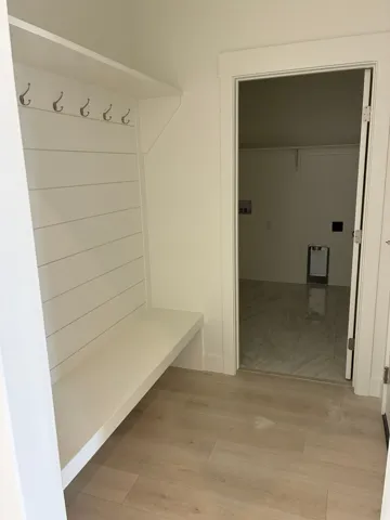 Built-in bench with shiplap backing and hanging hooks, wood-finish flooring, and a separate laundry area with tile flooring