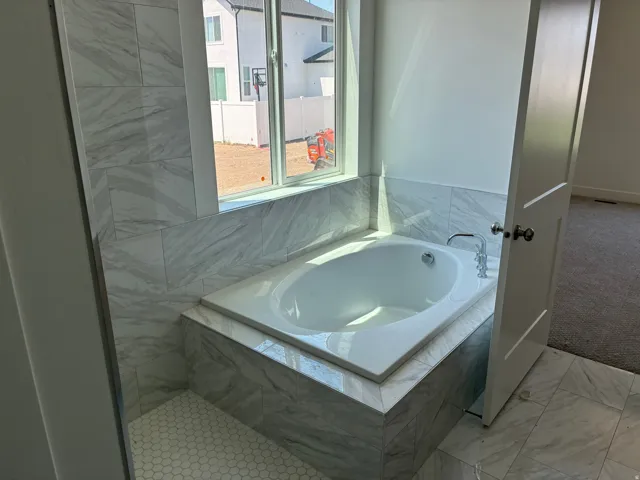Soaking tub with a polished chrome faucet, surrounded by large format tile, and hexagonal floor tile