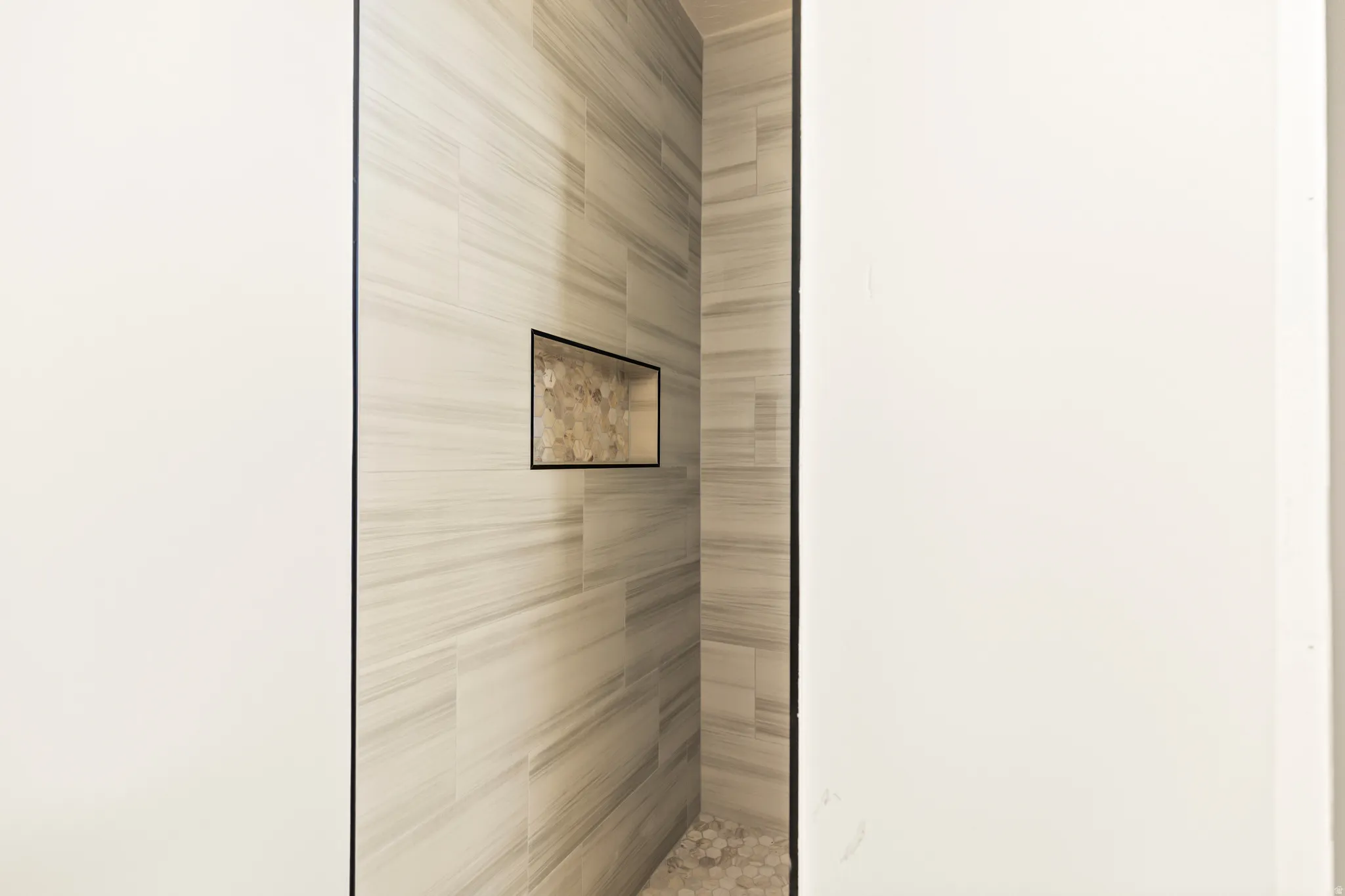 Tiled shower enclosure featuring a recessed niche and pebble-style flooring
