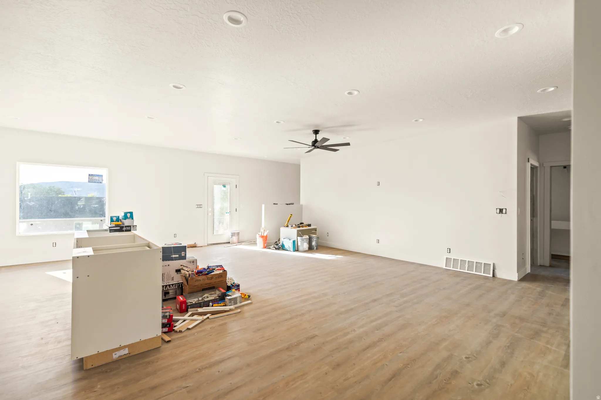 Spacious room featuring wood-finish flooring, white walls, recessed ceiling lights, and a ceiling fan