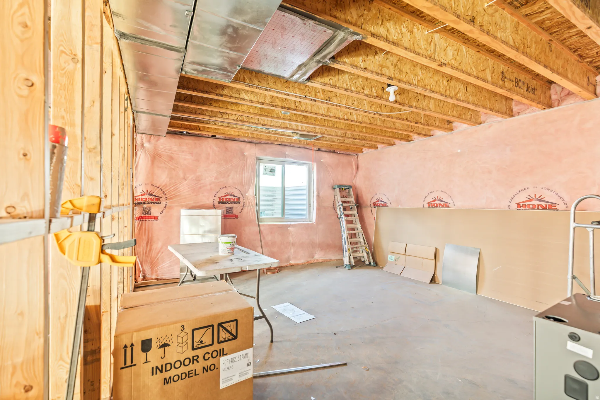Unfinished basement space with exposed wooden joists, insulated exterior walls, and a window opening