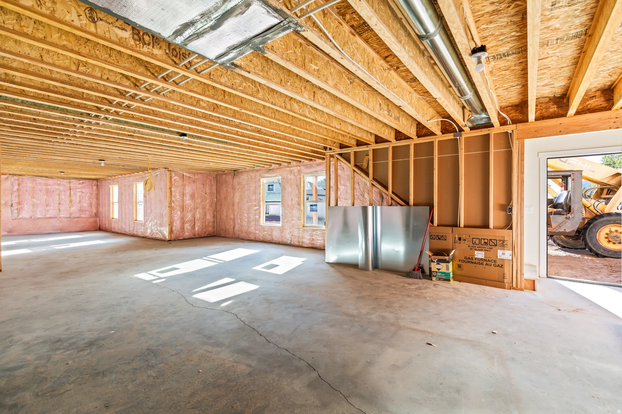 Exposed ceiling joists with visible subflooring, concrete flooring, insulated wall framing, multiple windows, and an open doorway