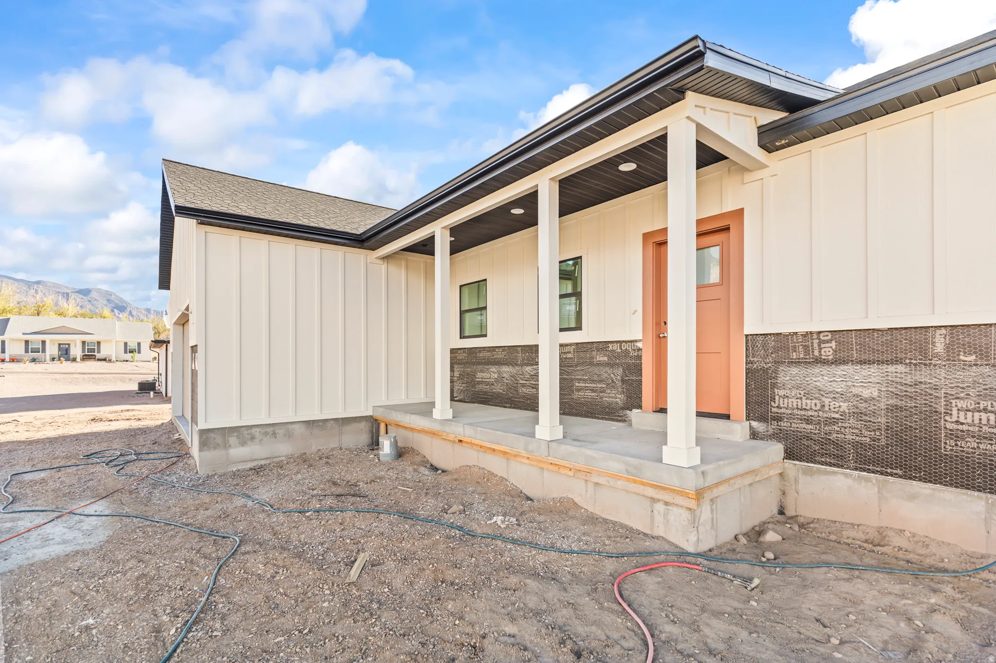 Front porch entry with a salmon-toned door, vertical board siding, and black trim accents