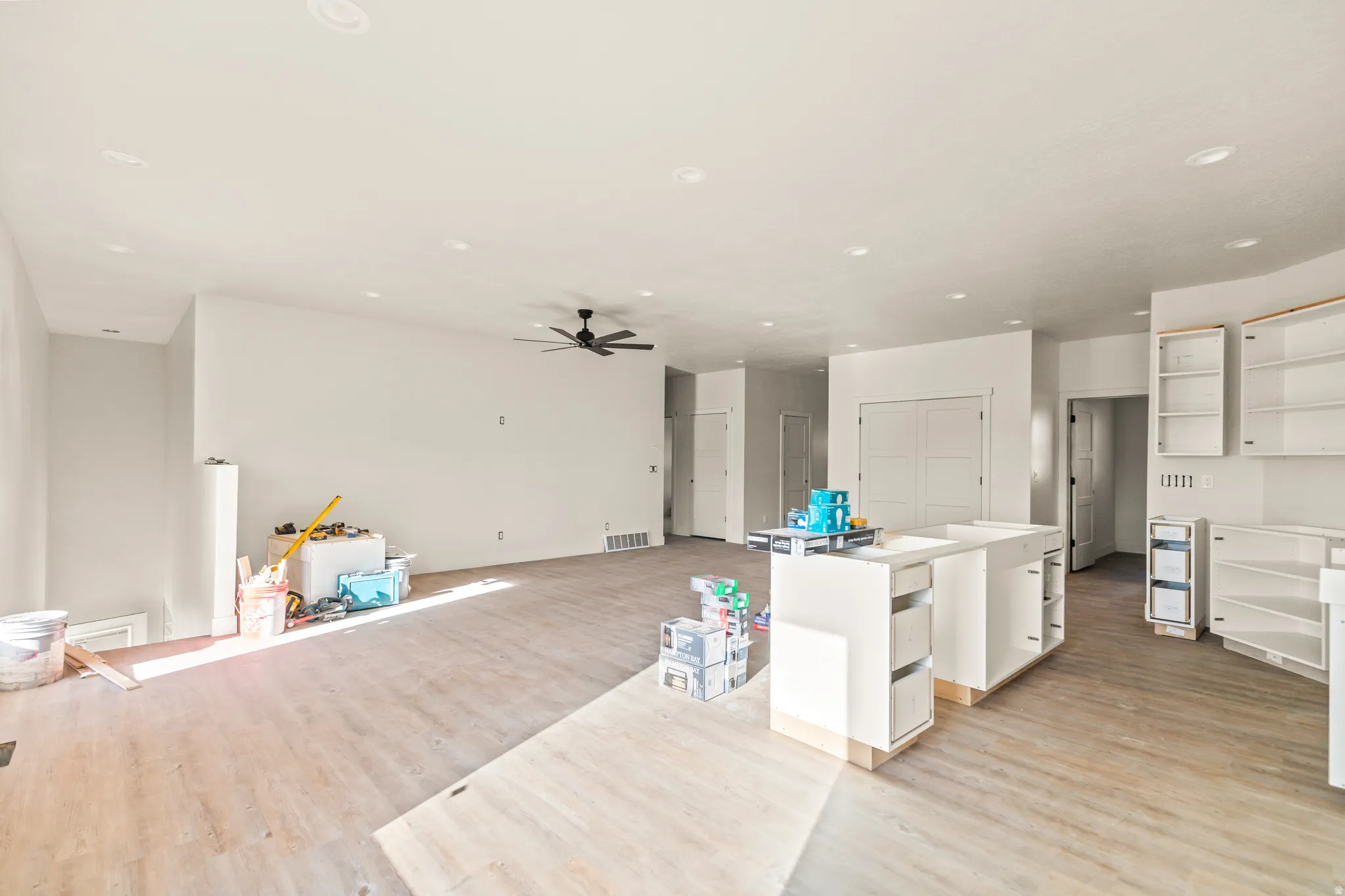 Recessed lighting, wood-finish flooring, ceiling fan, white cabinetry, and a kitchen island