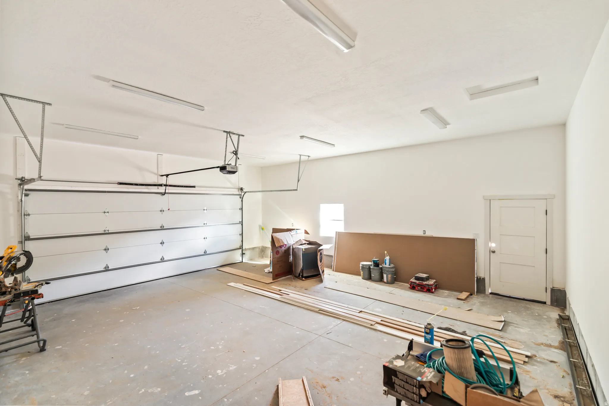 Spacious garage with an overhead door, concrete flooring, multiple overhead light fixtures, and a side entry door