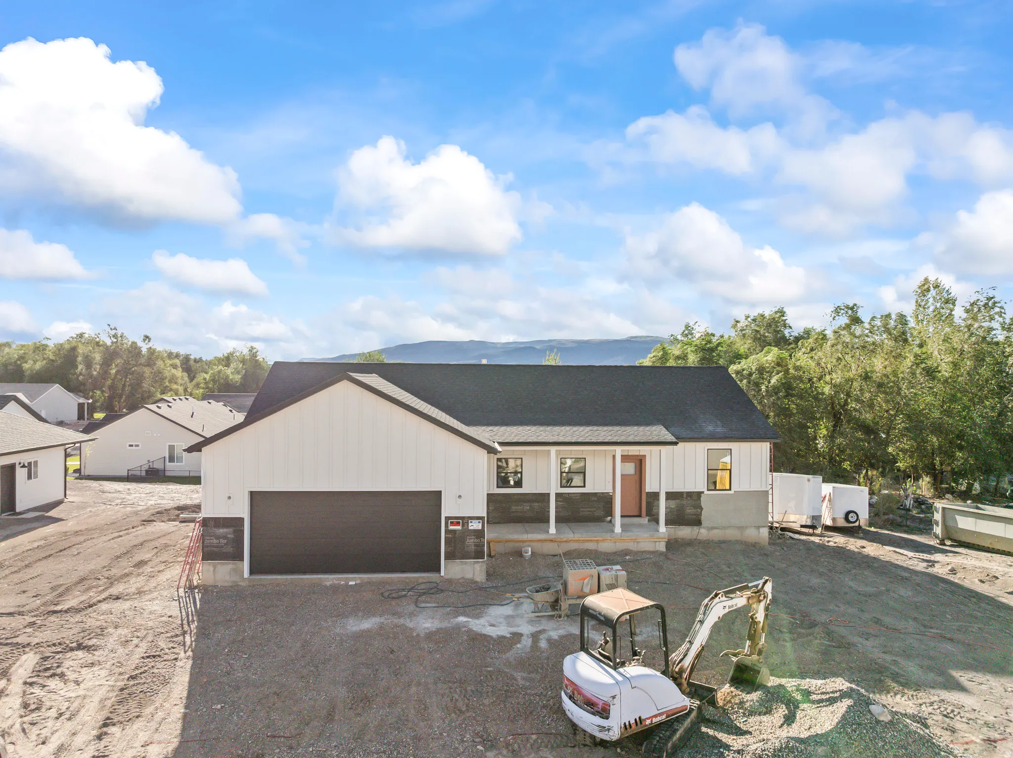 Modern farmhouse exterior with white vertical siding, dark roof, two-car garage, covered porch, and stone accents
