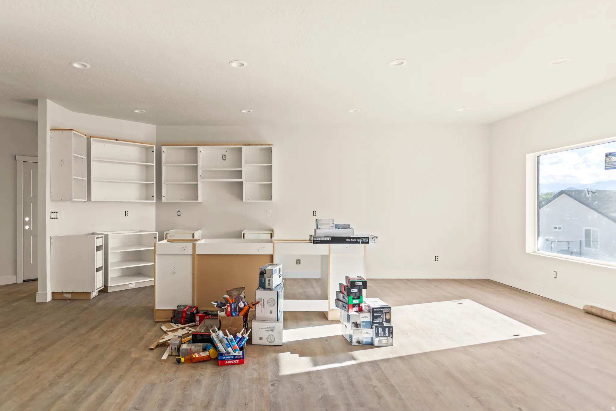 Recessed lighting, wood-finish flooring, white cabinetry, and a large window