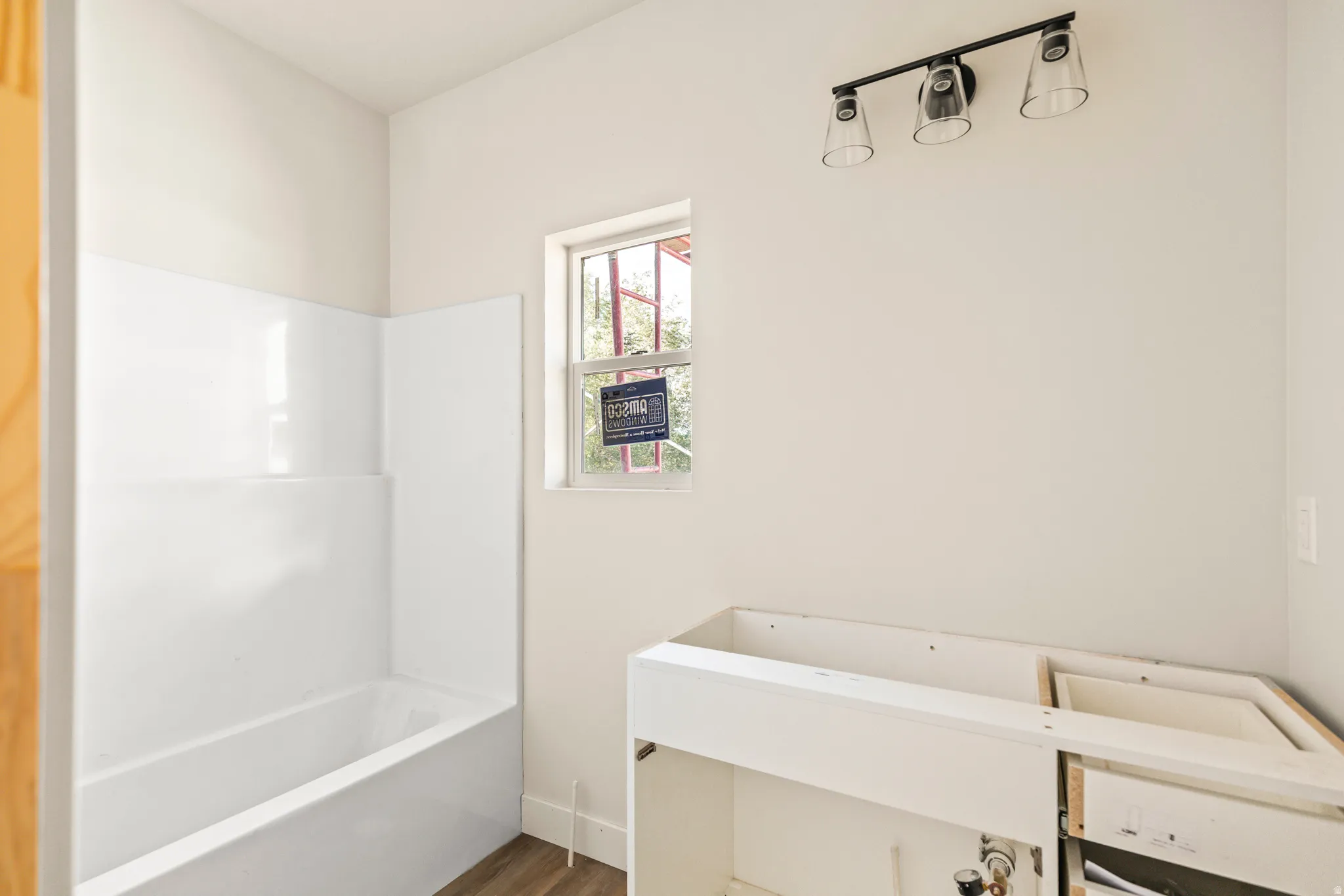 White acrylic tub and shower surround, window with white trim, and a black three-light vanity fixture