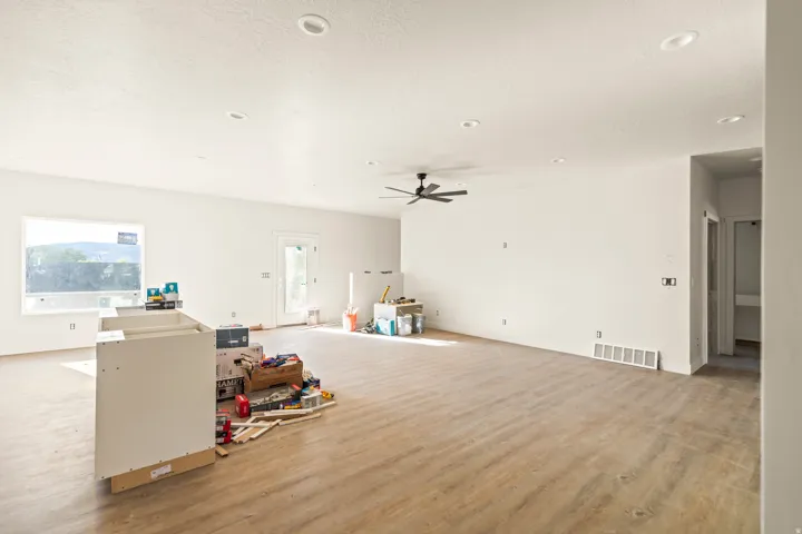 Spacious room featuring wood-finish flooring, white walls, recessed ceiling lights, and a ceiling fan