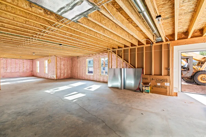 Exposed ceiling joists with visible subflooring, concrete flooring, insulated wall framing, multiple windows, and an open doorway