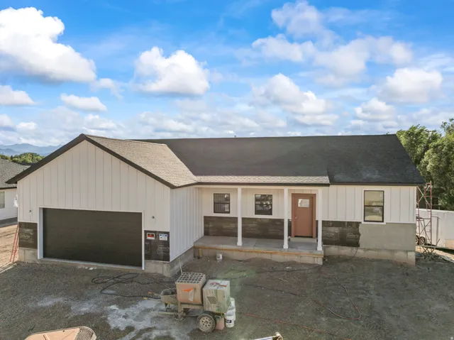 Board and batten siding with dark trim, covered front porch, dark shingle roof, attached garage with a dark door, and a brown entry door