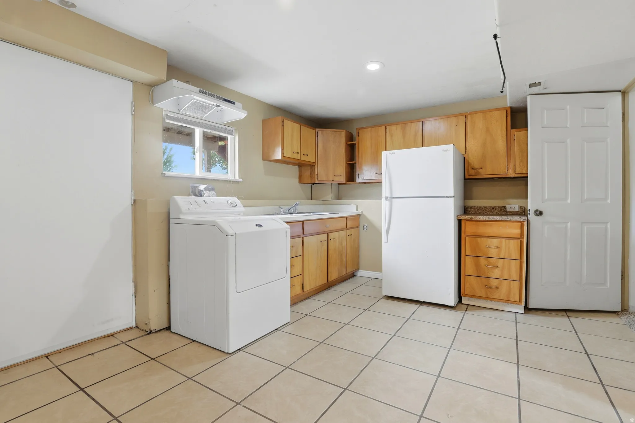 Kitchenette with wood-finish cabinetry, tile flooring, and a dryer. Electrical for an possible oven is behind the dryer.