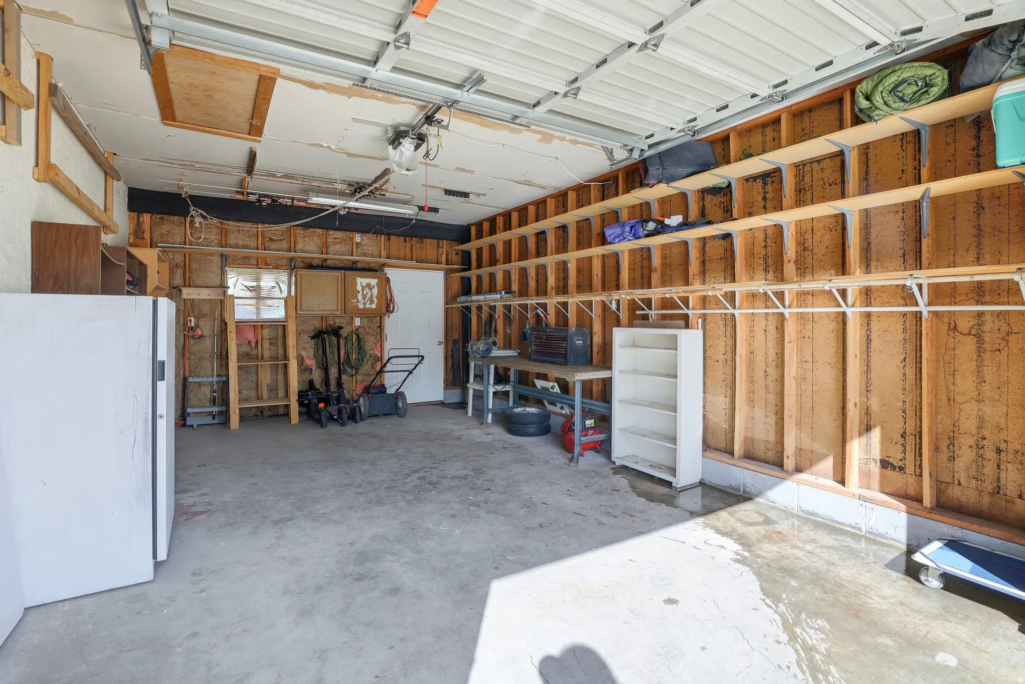 Attached garage with concrete flooring, overhead garage door, and built-in wall shelving