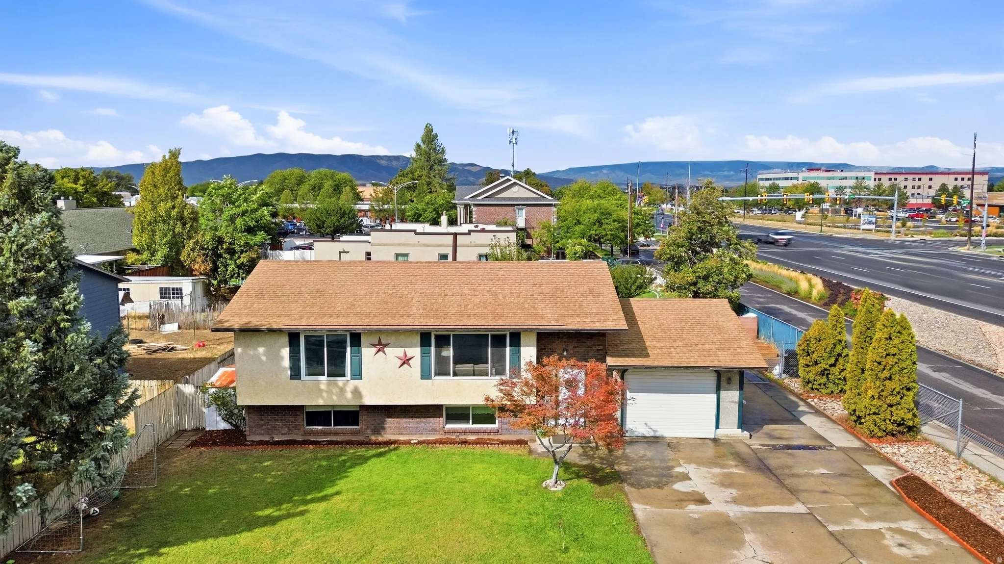 Manicured front lawn, mature trees, attached garage, and paved driveway