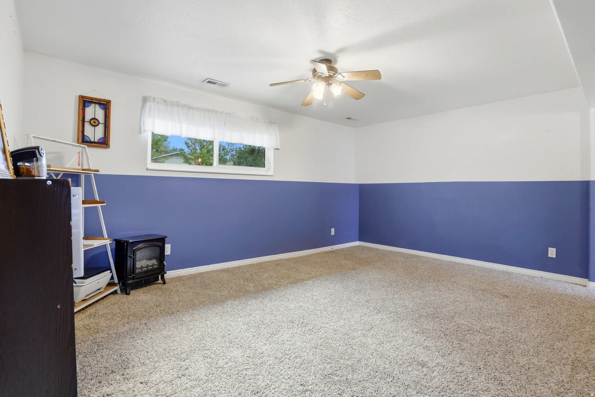Carpeted interior space with a ceiling fan, a window, and two-tone painted walls