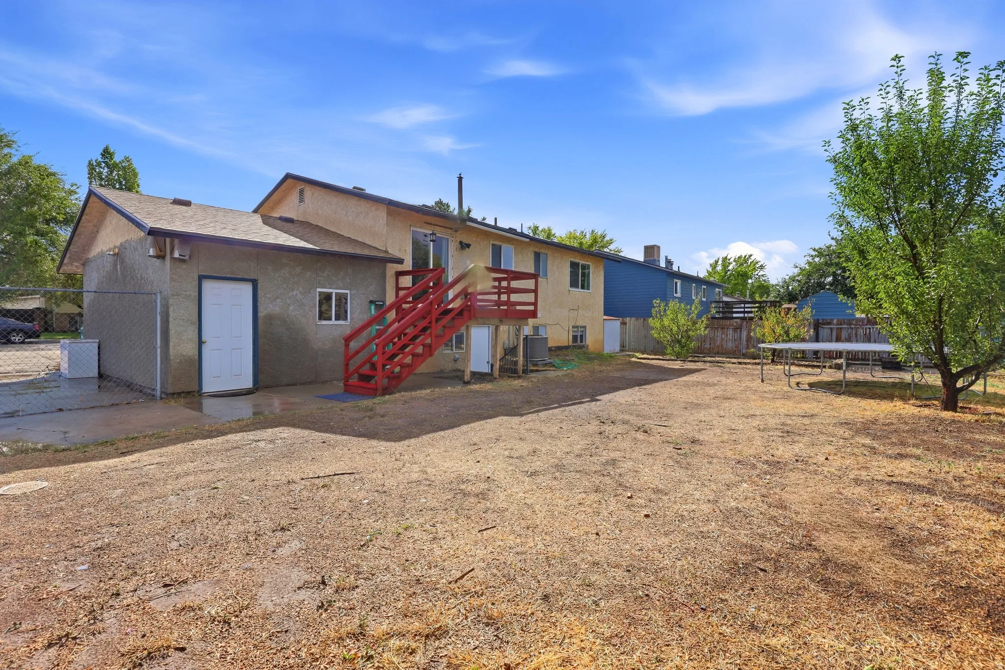 Rear exterior with a second-story deck, red-painted stairs, and a ground-level patio