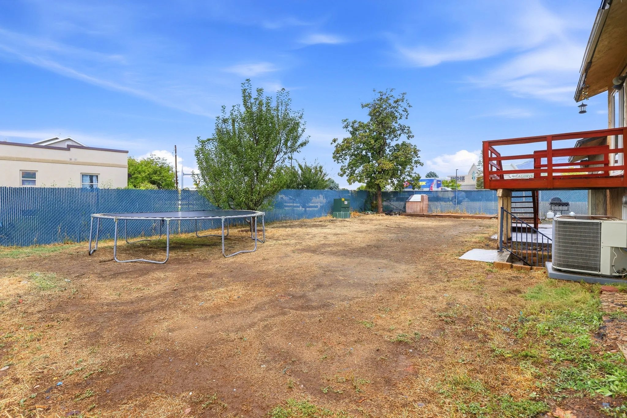Expansive backyard with a chain-link fence, mature trees, and an elevated wood deck with railing