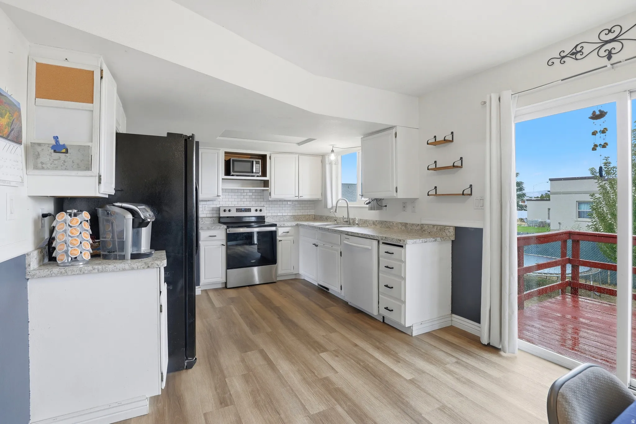 Kitchen featuring newer LVP flooring, white cabinetry, a tile backsplash, and a sliding glass door opening to an exterior deck
