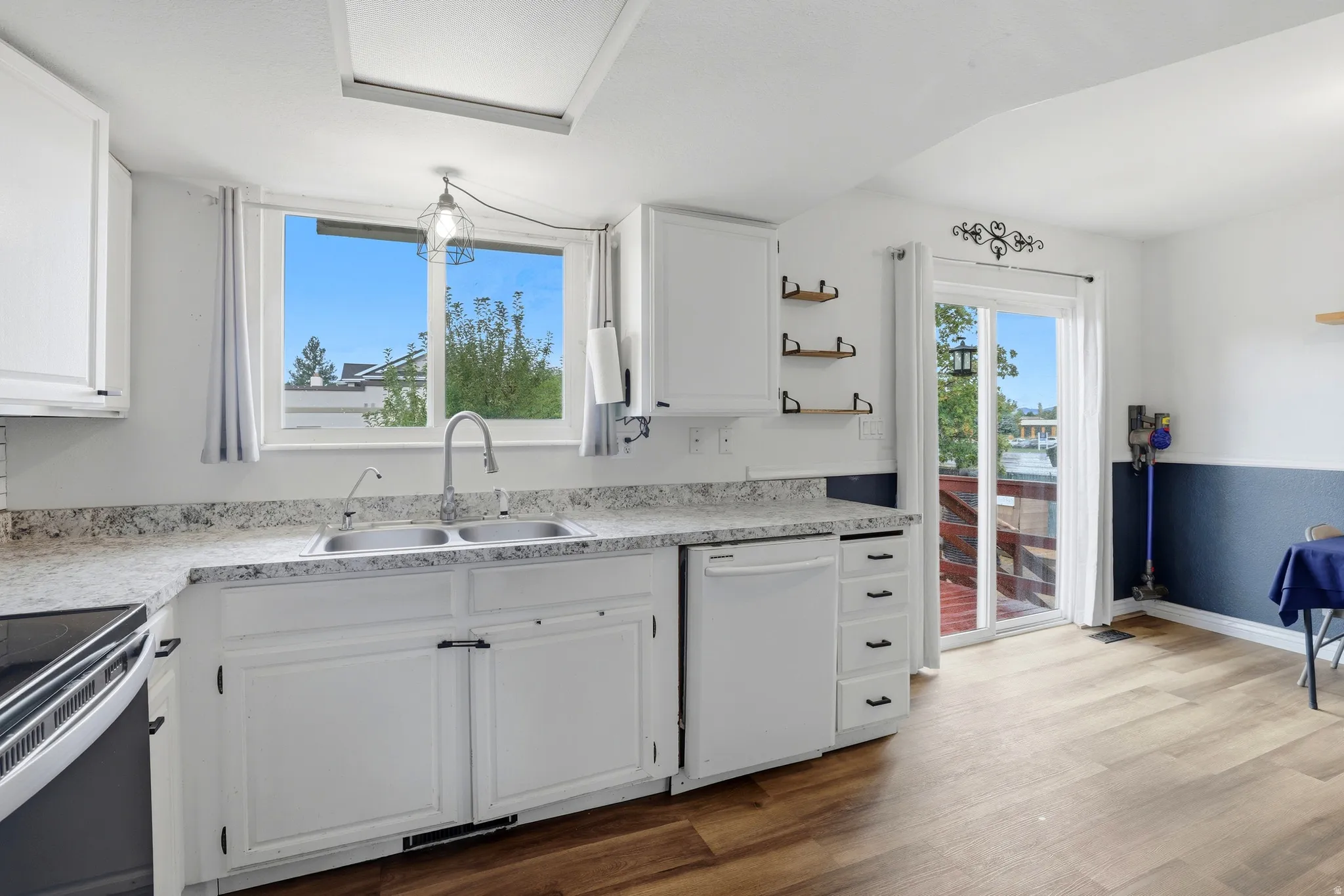 Kitchen featuring white cabinetry, light-toned countertops, a double basin sink with a gooseneck faucet, a white dishwasher, and wood-finish flooring