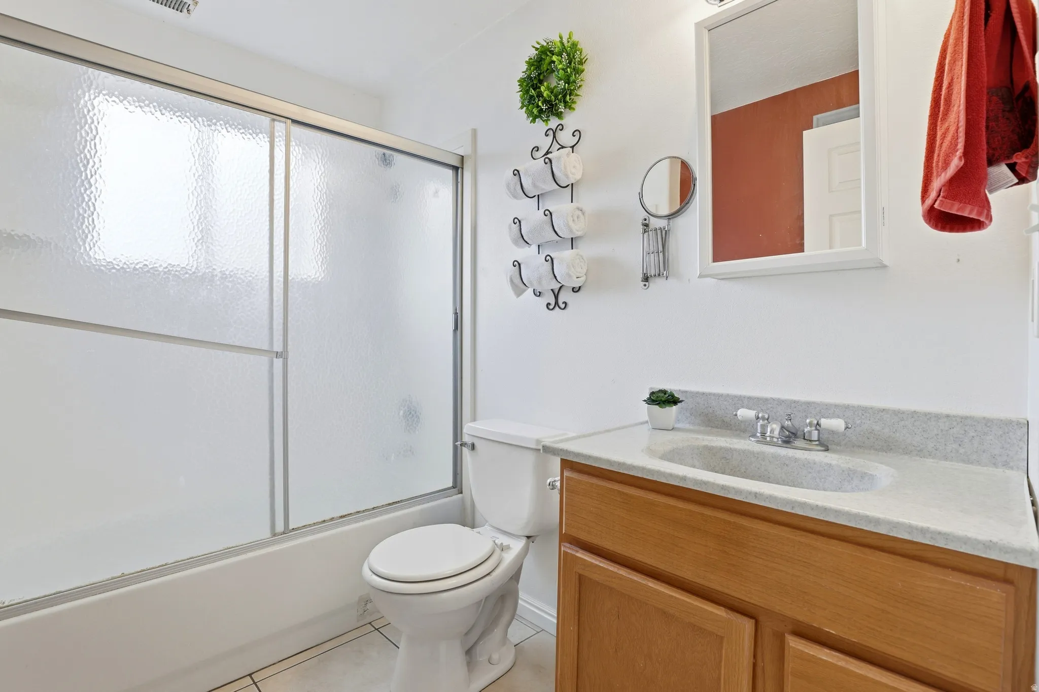 Bathtub with sliding frosted glass enclosure, toilet, wood-finish vanity with an integrated sink, and a wall-mounted mirror