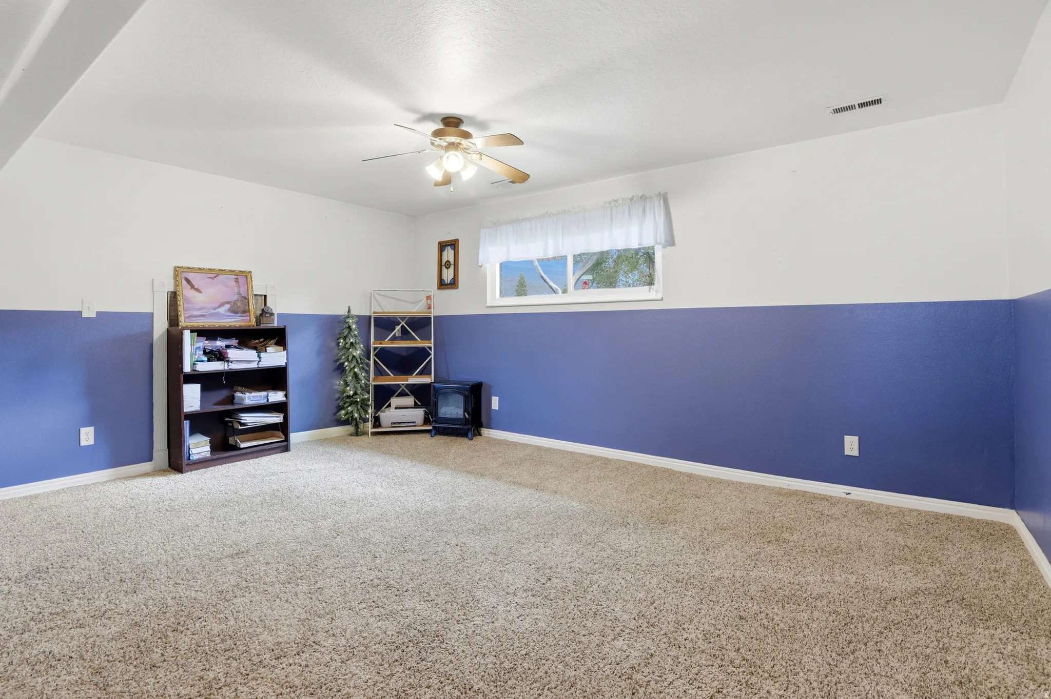 Carpeted flooring, ceiling-mounted light fixture, white and blue painted walls, and a single window