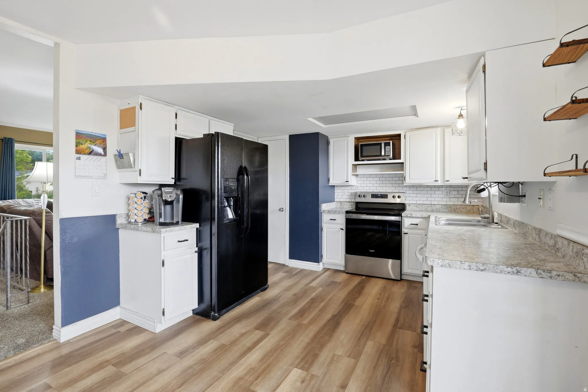 Kitchen featuring newer LVP flooring, white cabinetry, light-toned countertops, subway tile backsplash, and stainless steel appliances