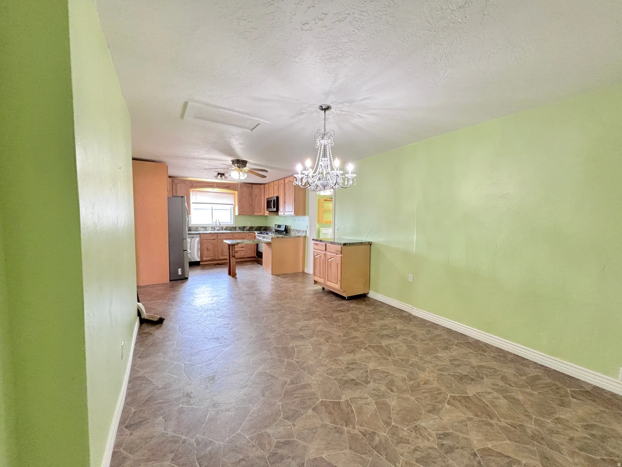 Open concept living and kitchen areas featuring wood-finish cabinetry, tile-look flooring, and a chandelier lighting fixture