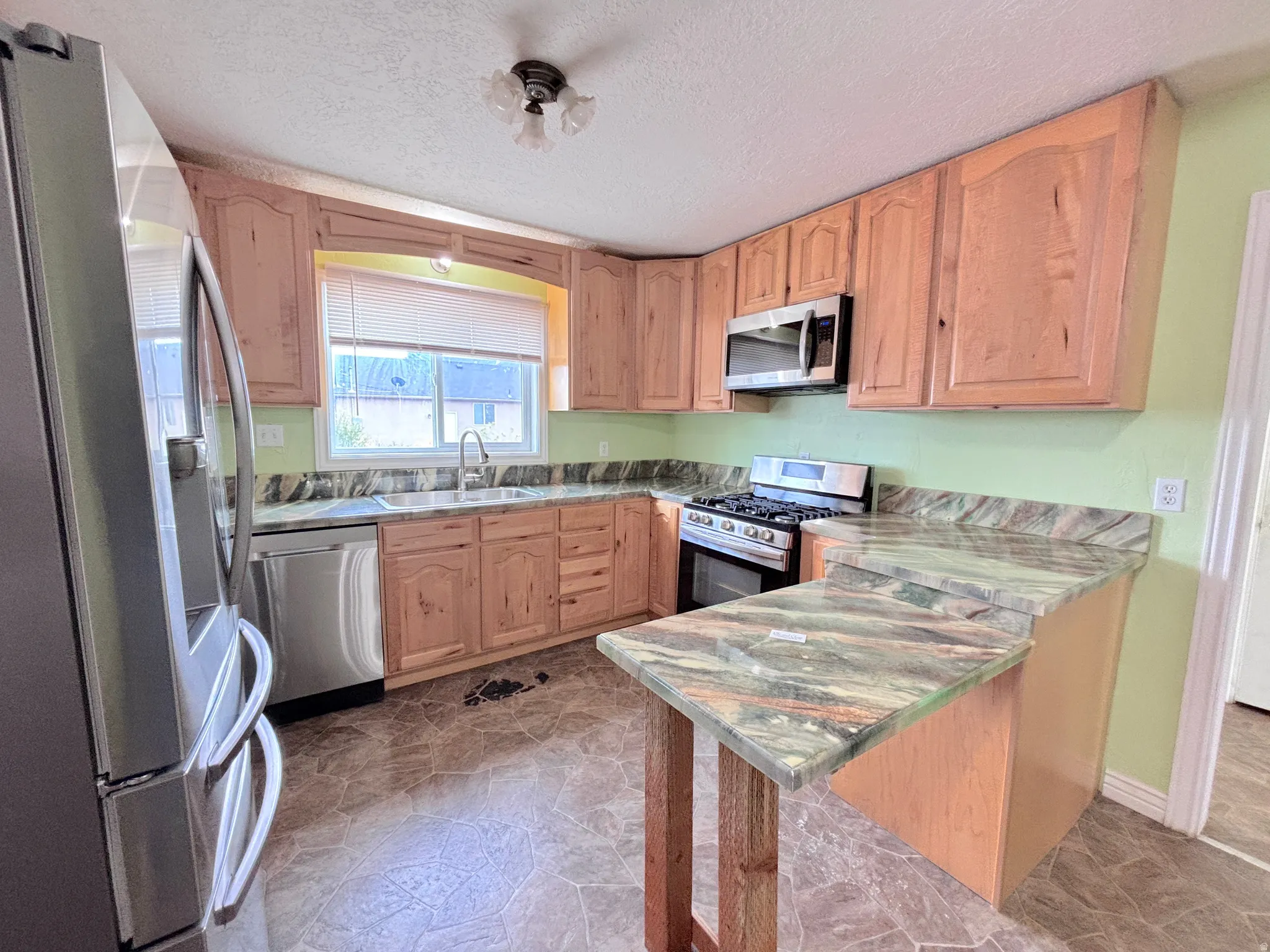 Kitchen featuring wood cabinetry, a stainless steel gas range, microwave, and dishwasher, stone-finish countertops, and an integrated breakfast bar