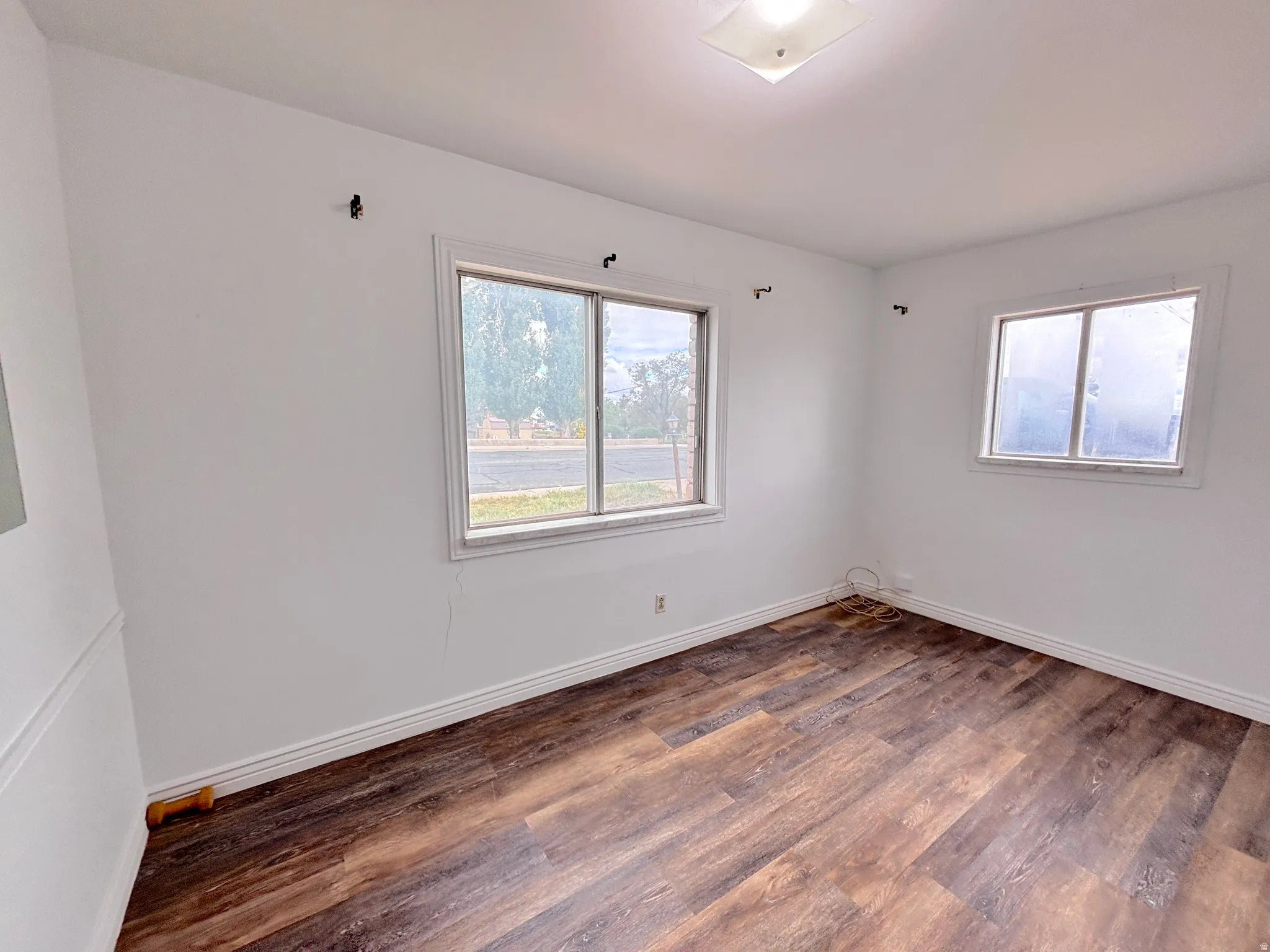 Wood-finish flooring with white baseboards, white walls, and a ceiling-mounted light fixture