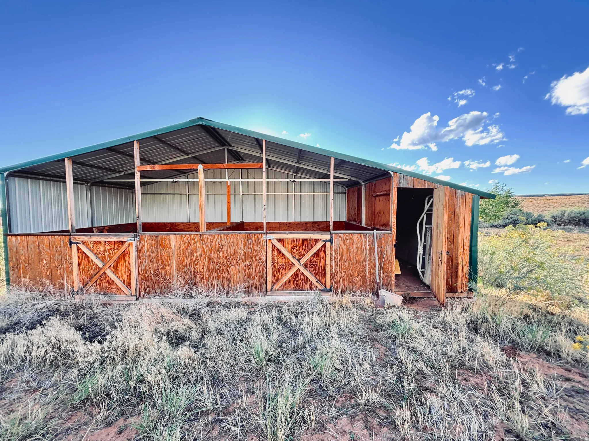 Freestanding barn structure featuring a green metal roof, multiple stalls with wooden gates, metal siding, and a rustic wood finish on the exterior
