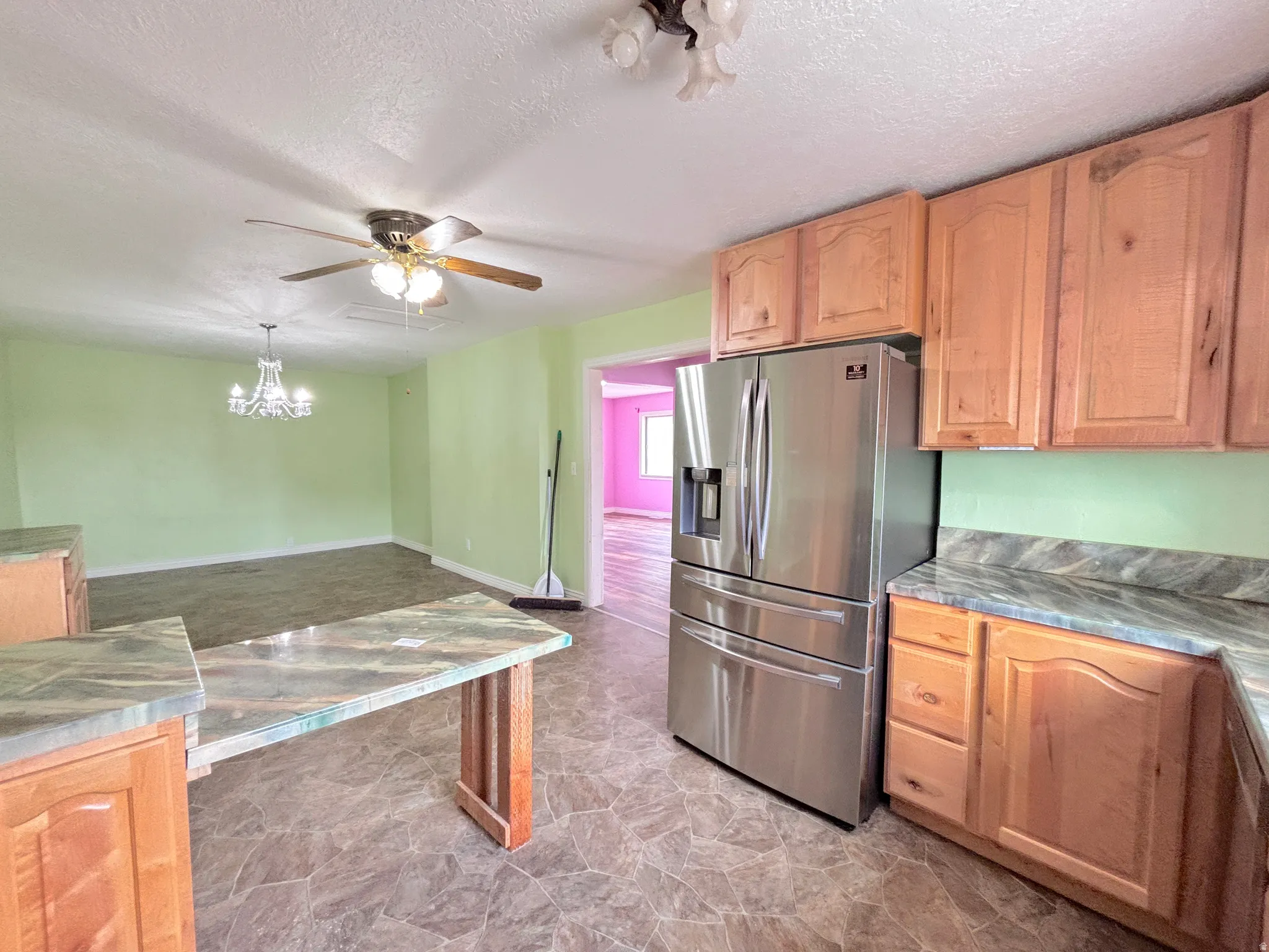 Kitchen featuring wood-finish cabinetry, stone-look countertops, stainless steel refrigerator, and tile flooring