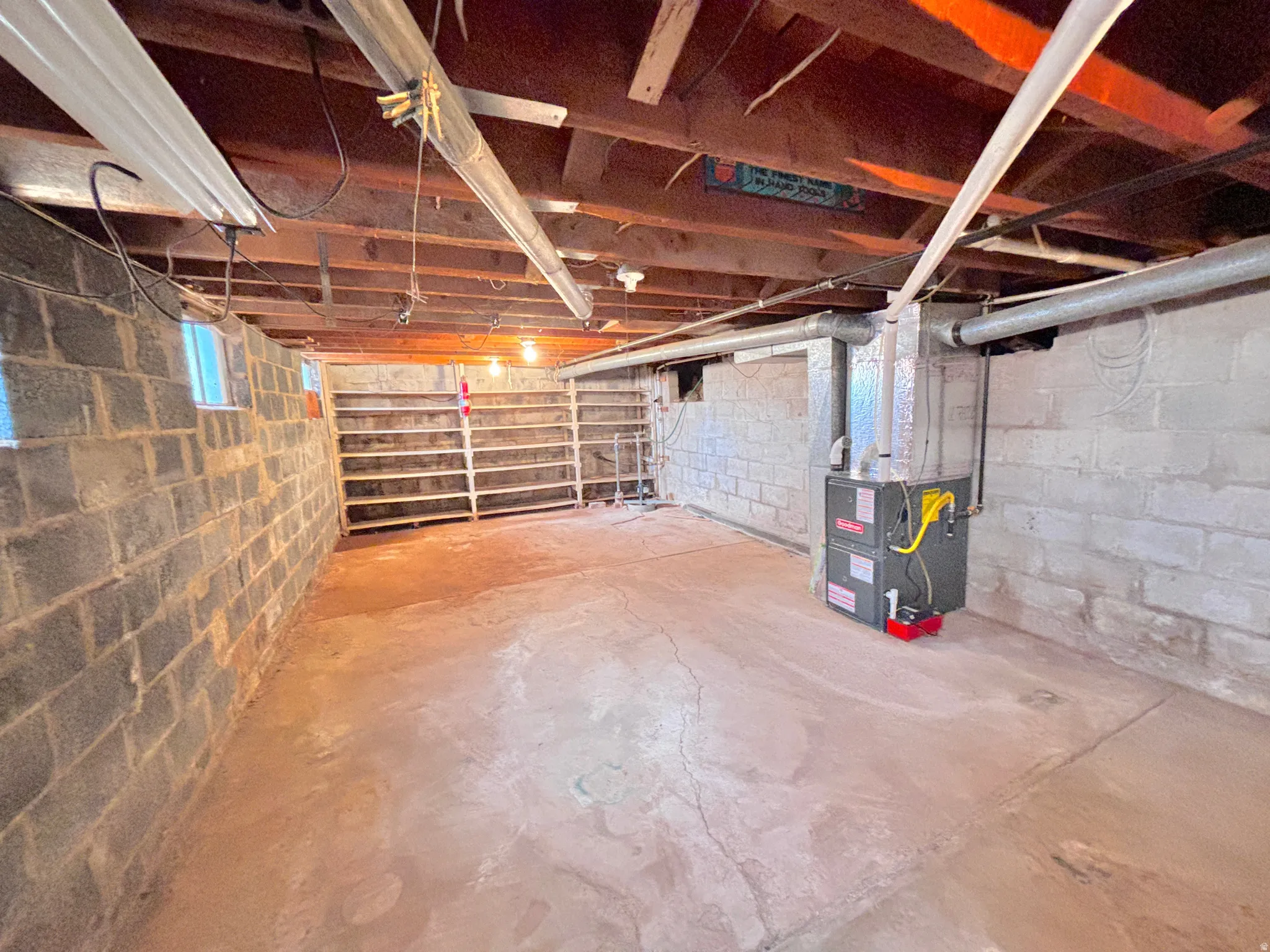 Basement space featuring concrete block walls, exposed wood ceiling joists, and a forced-air furnace