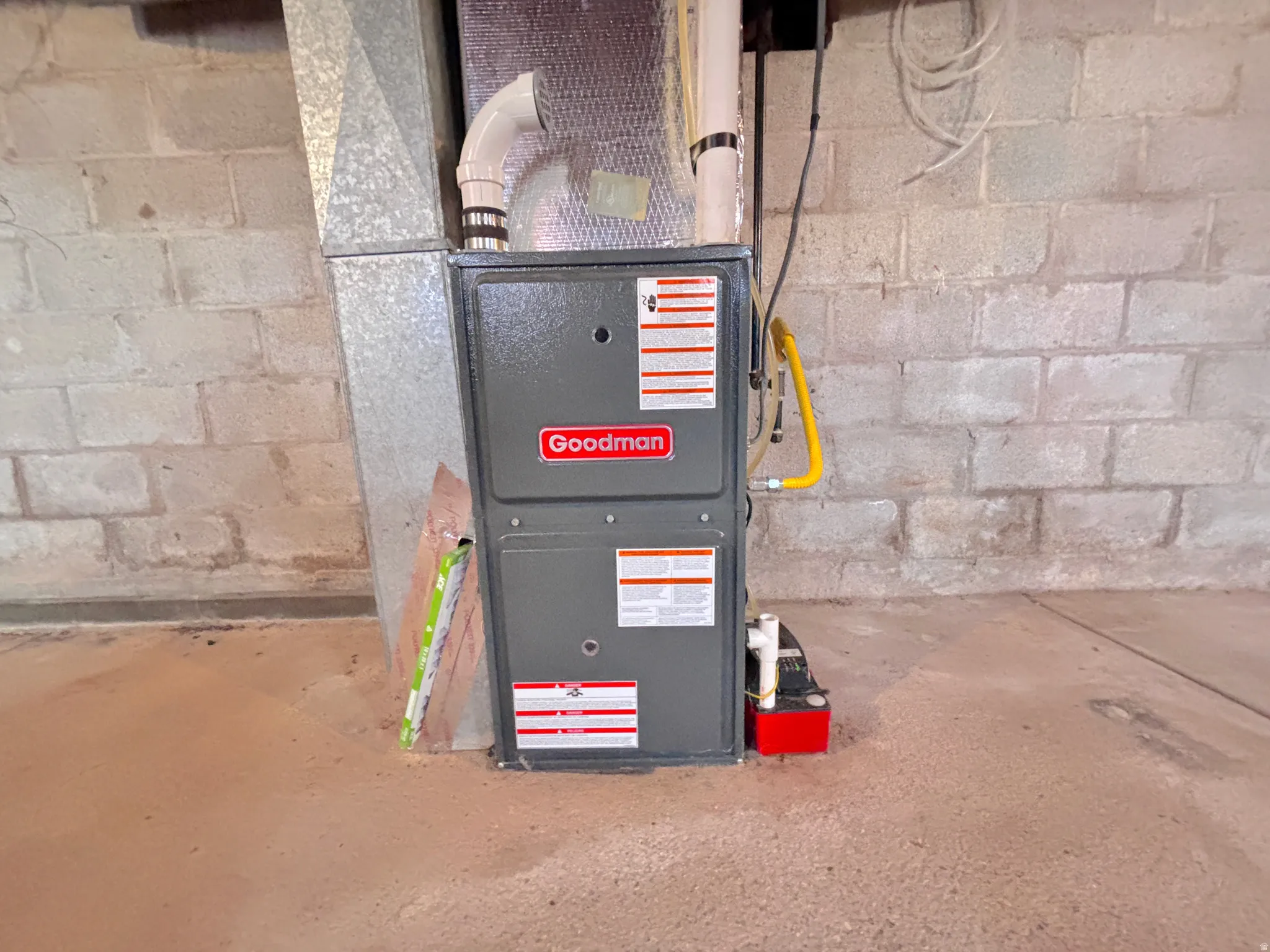 Goodman brand furnace with attached condensate pump, set against a concrete block wall and finished concrete floor