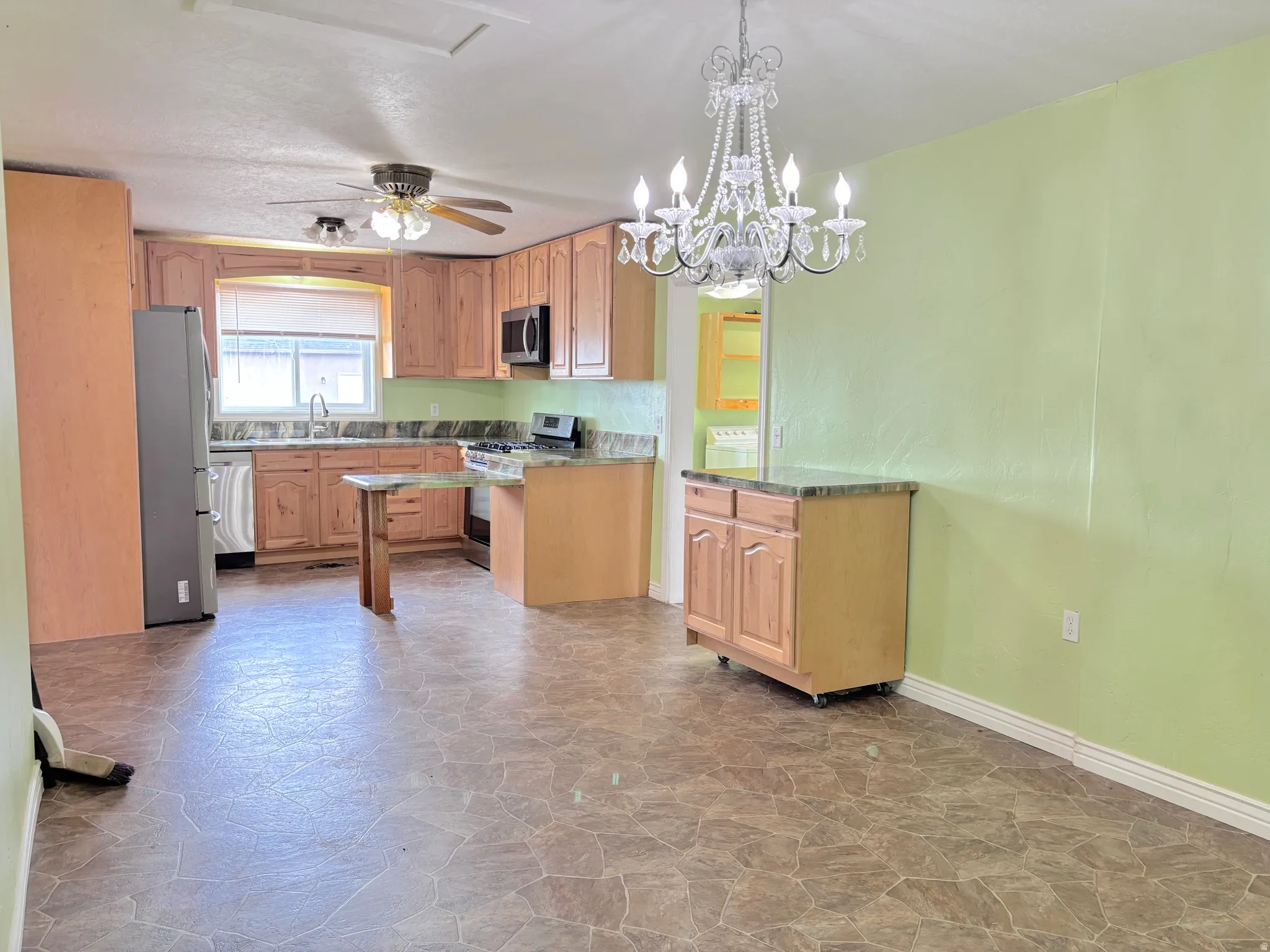 Kitchen featuring wood cabinetry, stainless steel appliances, a ceiling fan, and a chandelier
